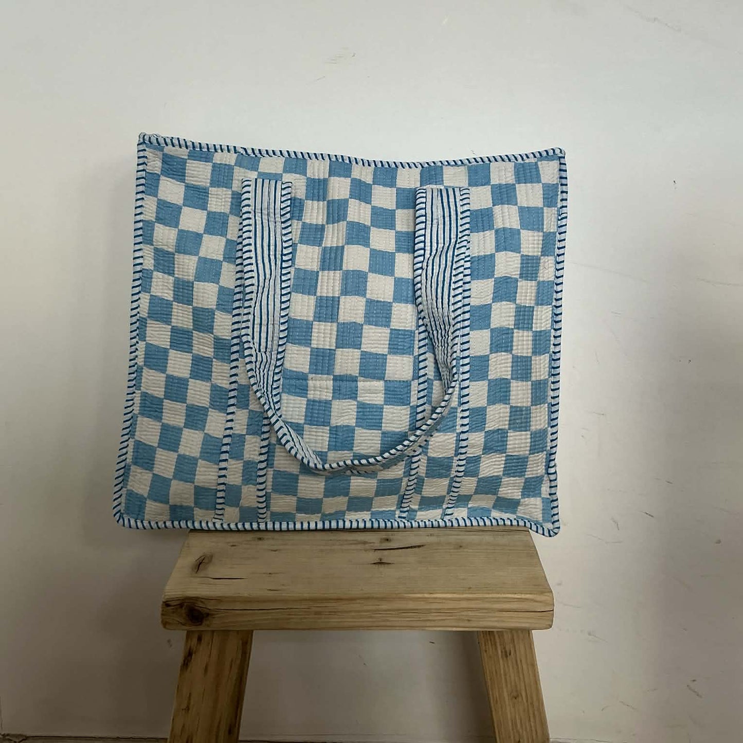 Blue and white checkered bag on a wooden stool against a white wall