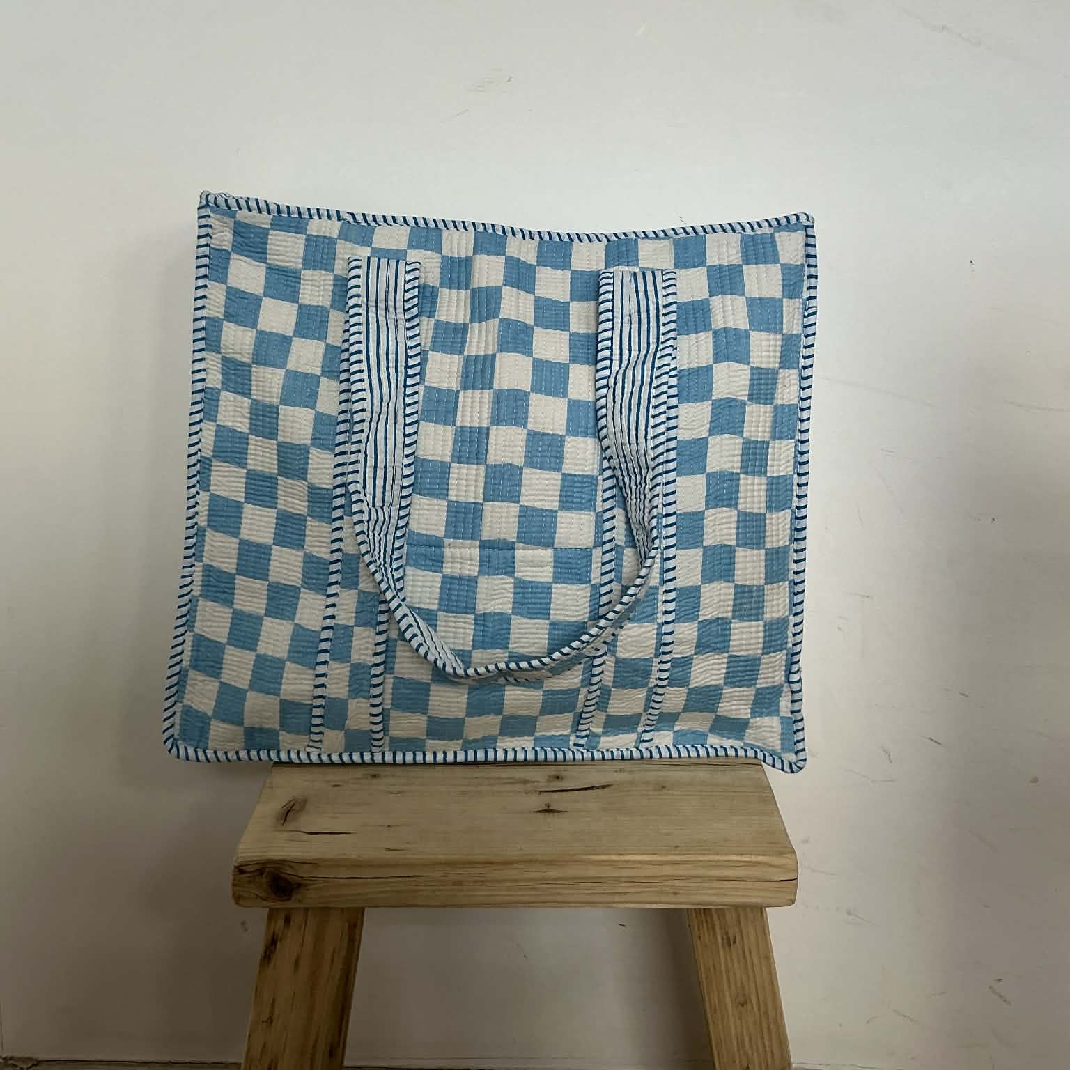 Blue and white checkered bag on a wooden stool against a white wall
