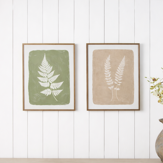 Two framed botanical prints on a wall above a wooden cabinet with a vase of flowers.