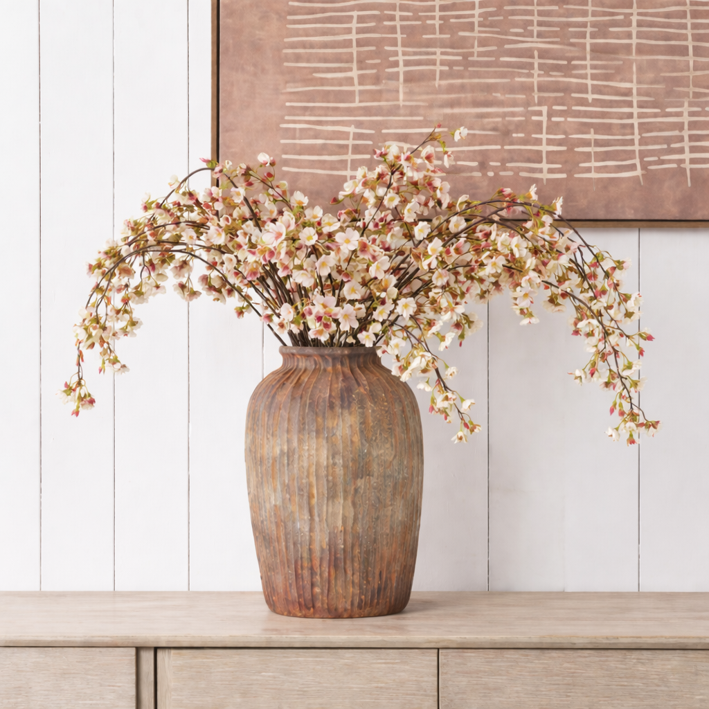 Decorative vase with floral branches on a wooden surface against a white wall.
